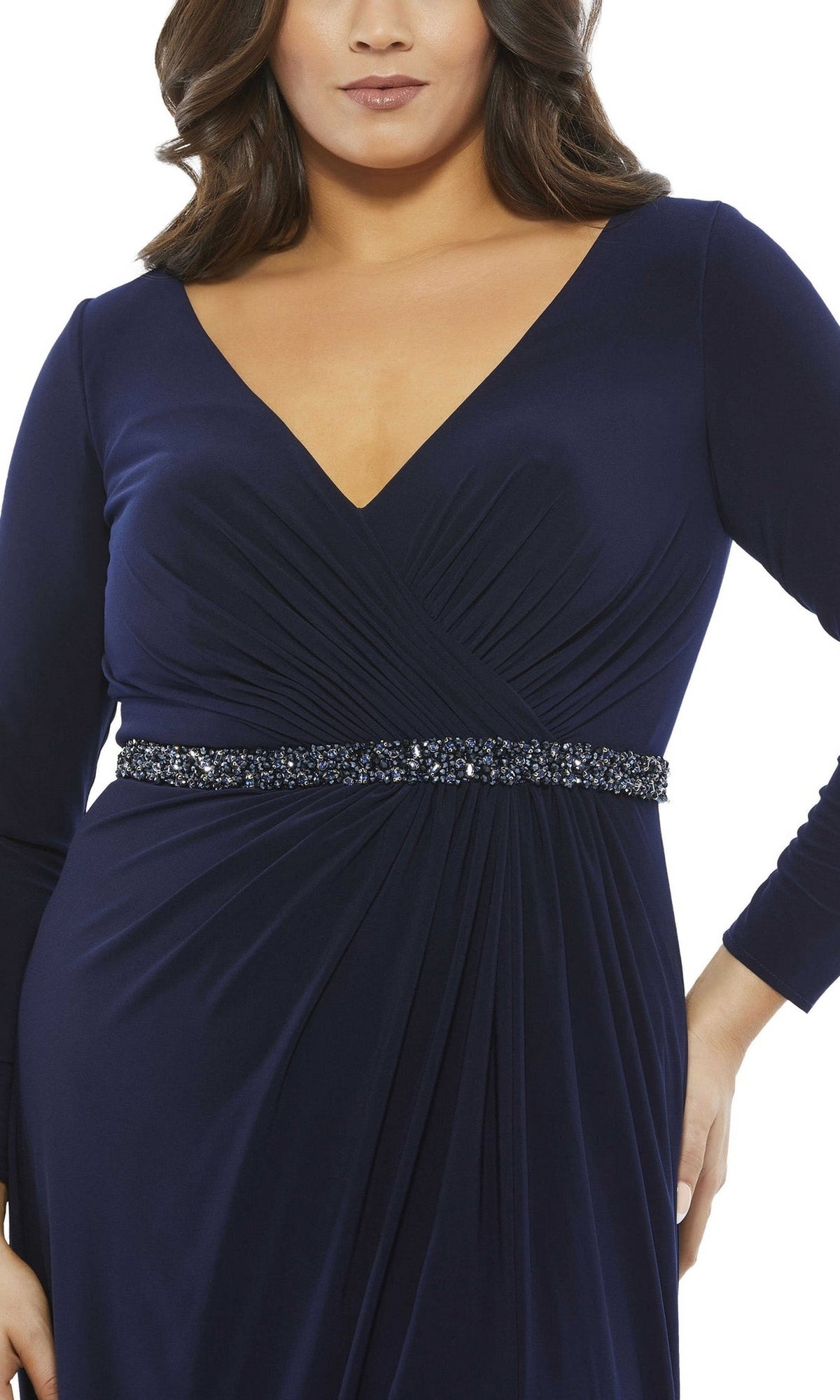 A woman in the Mac Duggal Long Plus-Size Prom Dress 67899, a navy blue gown with long sleeves, a deep V-neckline, and a beaded waistband.